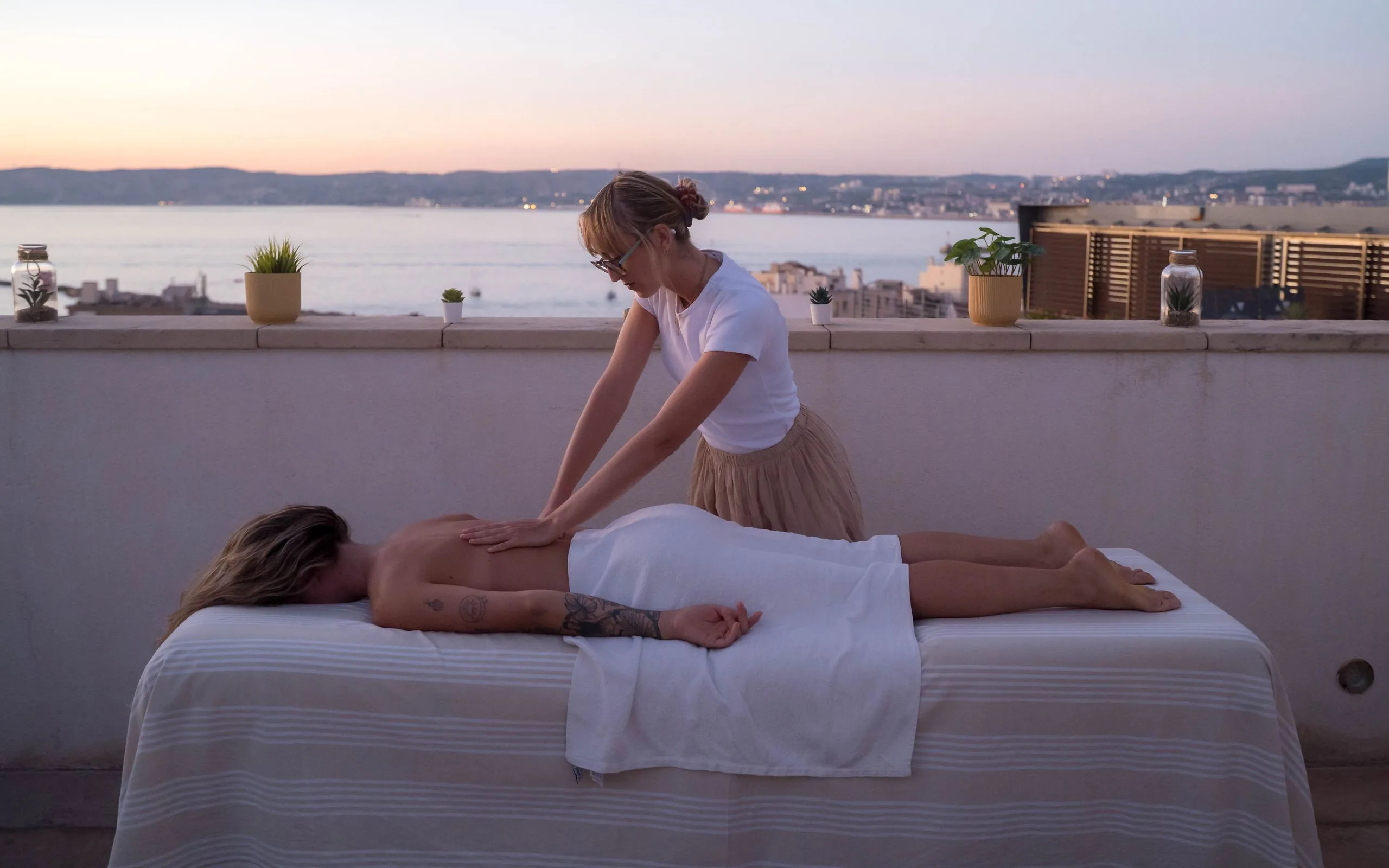 Chiara Maziere pratiquant un massage bien-être sur une terrasse face à la mer, au coucher du soleil