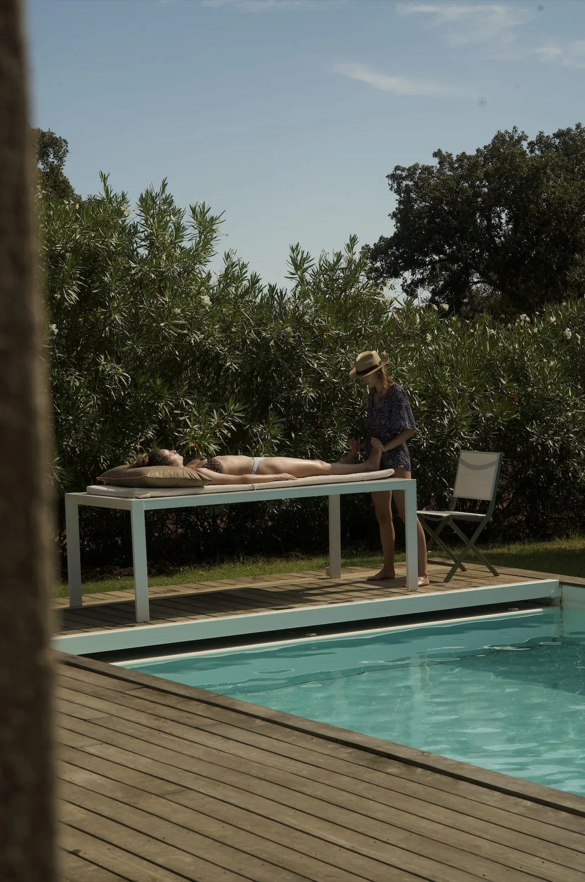 Chiara pratiquant la réflexologie plantaire sur une personne allongée, au bord d'une piscine